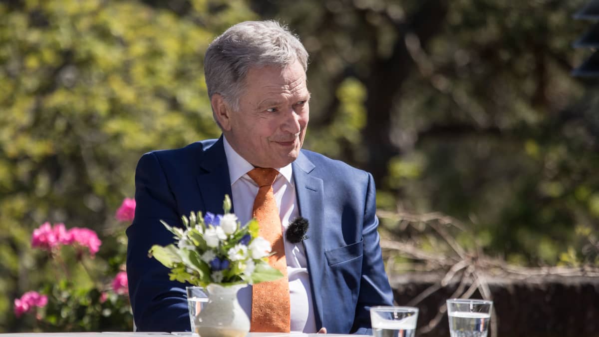 Leende Sauli Niinistö ute i solen bland blommorna på Gullranda.