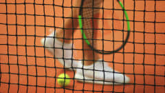Närbild på en person med tennisskor och tennisracket.