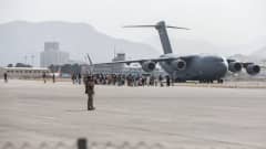  Flygfältet i Kabul. En folksamling framför en Air Force Boeing C-17. Soldater övervakar.