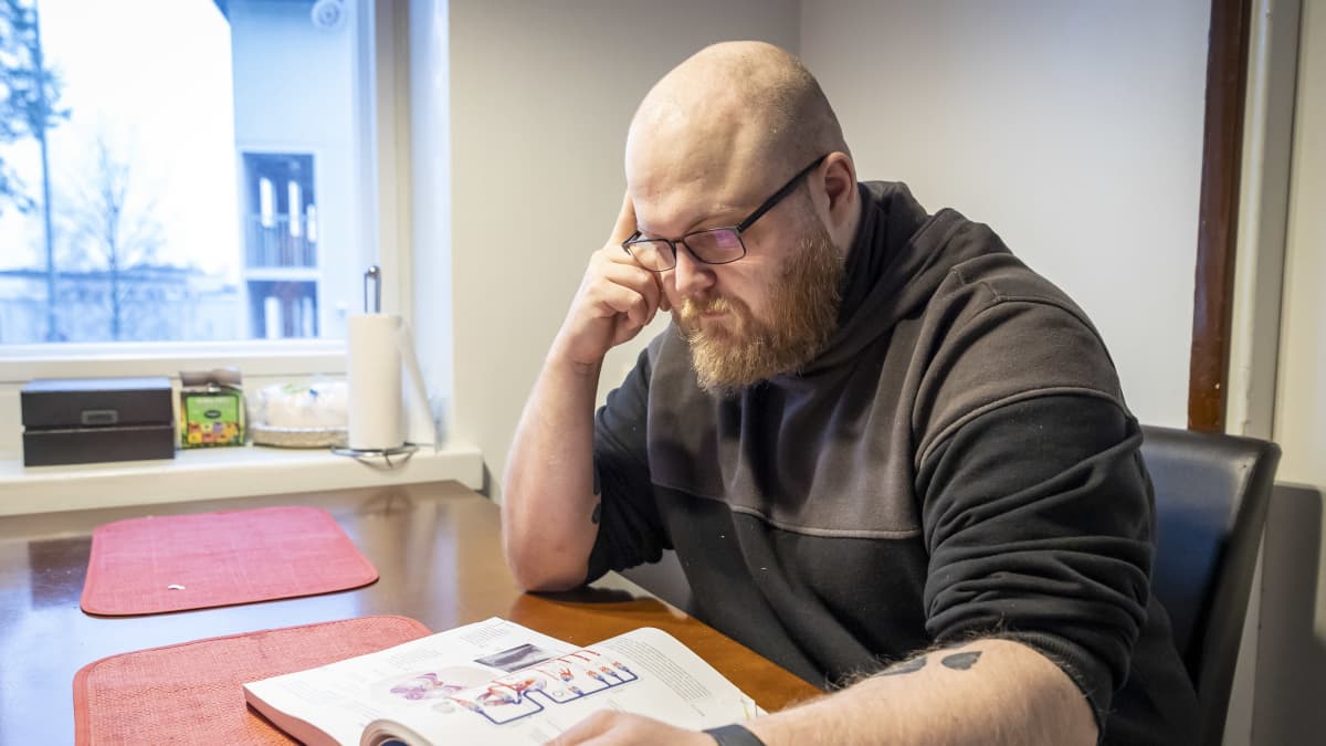 Janne Ostonen lukee oppikirjaa keittiön pöydän ääressä.