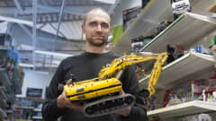 Jani Kuopio seisoo lego-kaupassa. Hän kannattelee legoista kokoamaansa kaivinkonetta kaksin käsin. 