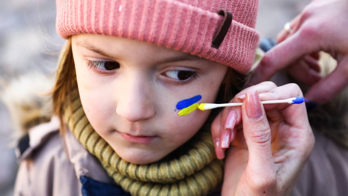 Pienen lapsen poskeen maalataan Ukrainan lippua.