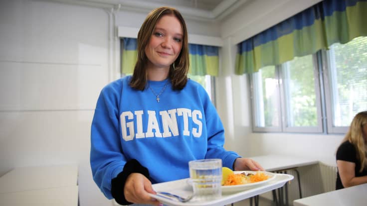 Hirvelän koulun oppilas Siiri Tankka pitelemässä tarjotinta, jossa on kouluruokaa lautasella sekä vesilasi.