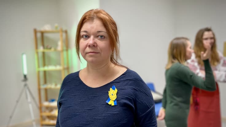 Olena Herasymenko, Suomen Ukrainalaiset ry:n puheenjohtaja katsoo kohti kameraa rinnassaan ukrainan väreissä oleva koriste.