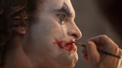 Närbild då Arthur (Joaquin Phoenix) sminkar sig till clown samtidigt som han gråter och blå mascara rinner nerför kinden.