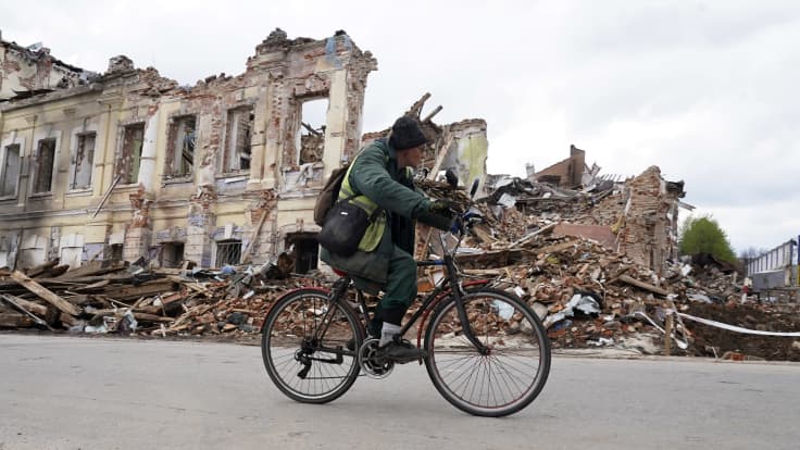 Henkilö pyöräilee tuhoutuneen rakennuksen vieressä.