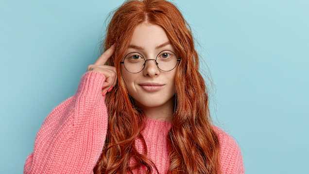 Kvinna med glasögon rör sitt huvud med fingret.