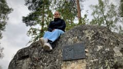 Mustasaarelainen Paula Jaskari istuu ison kiven päällä vanhan kyläkoulunsa pihalla.