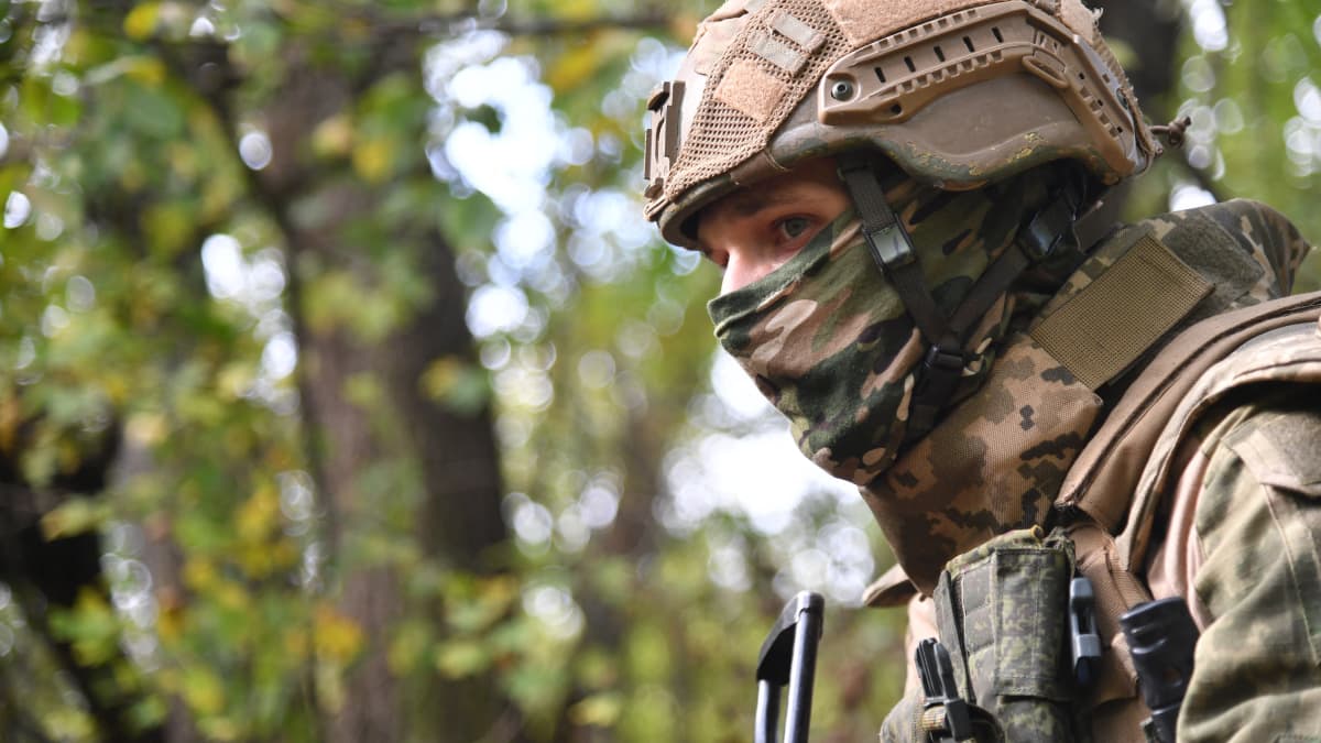 Sotilas univormussa ja kypärässä, naama peitetty maastokuvioisella huivilla. 