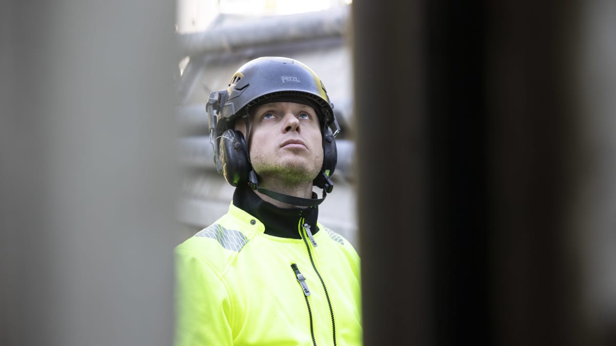 Poraaja Antti Roth katsoo kohti kallioporan yläosaa työvaatteet ja sininen kypärä yllään.