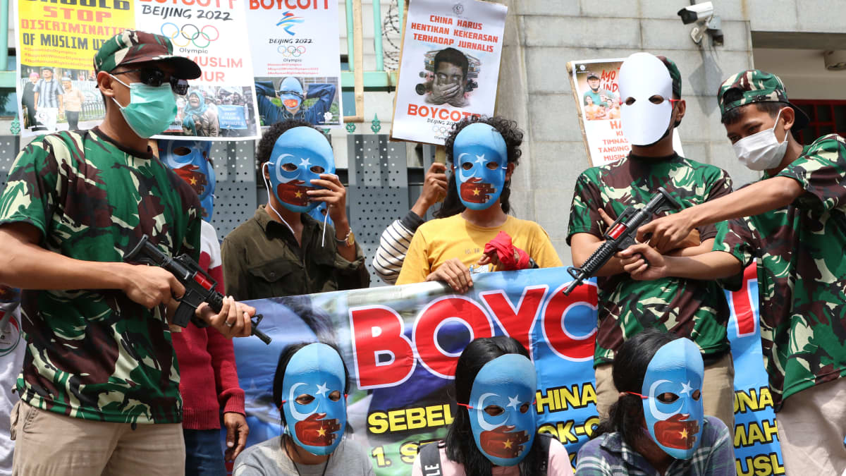 Mielenosoittajat vastustavat Pekingin olympialaisia. Heillä on kasvot peittävät siniset naamiot, sillä vaaleansininen väri viittaa uiguureihin. Osa on pukeutunut armeijakuosiin ja kantaa leikkiaseita.