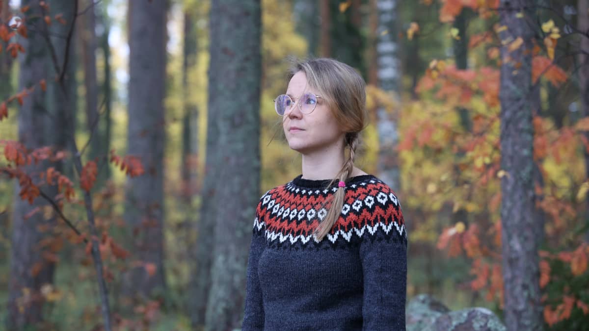 Camilla Nissinen seisoo metsässä, taustalla puita ruskan väreissä.