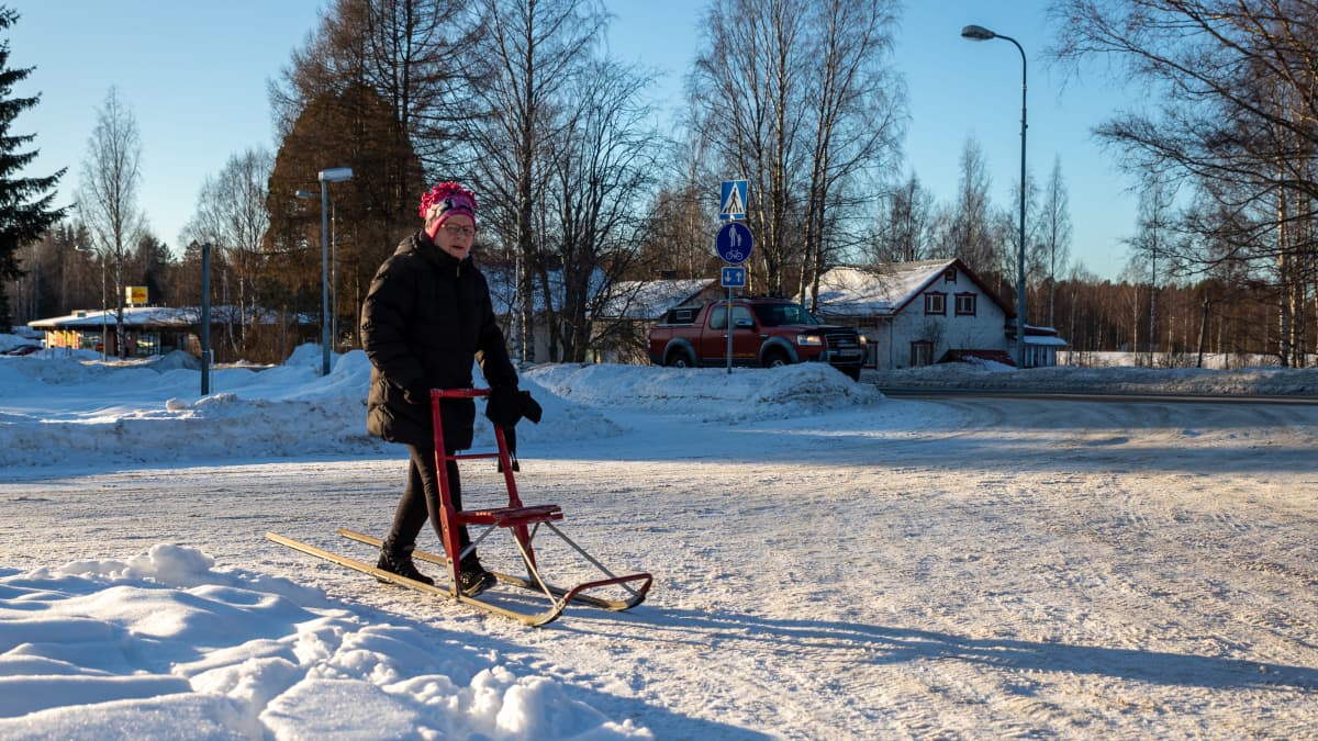 Nainen kulkee potkukelkan kanssa Kannonkosken kylänraitilla aurinkoisena talvipäivänä.