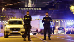 Kaksi poliisia seisoo varoitusnauhan takana suljetulla kadulla Brysselissä, taustalla kaupungin valoja. 