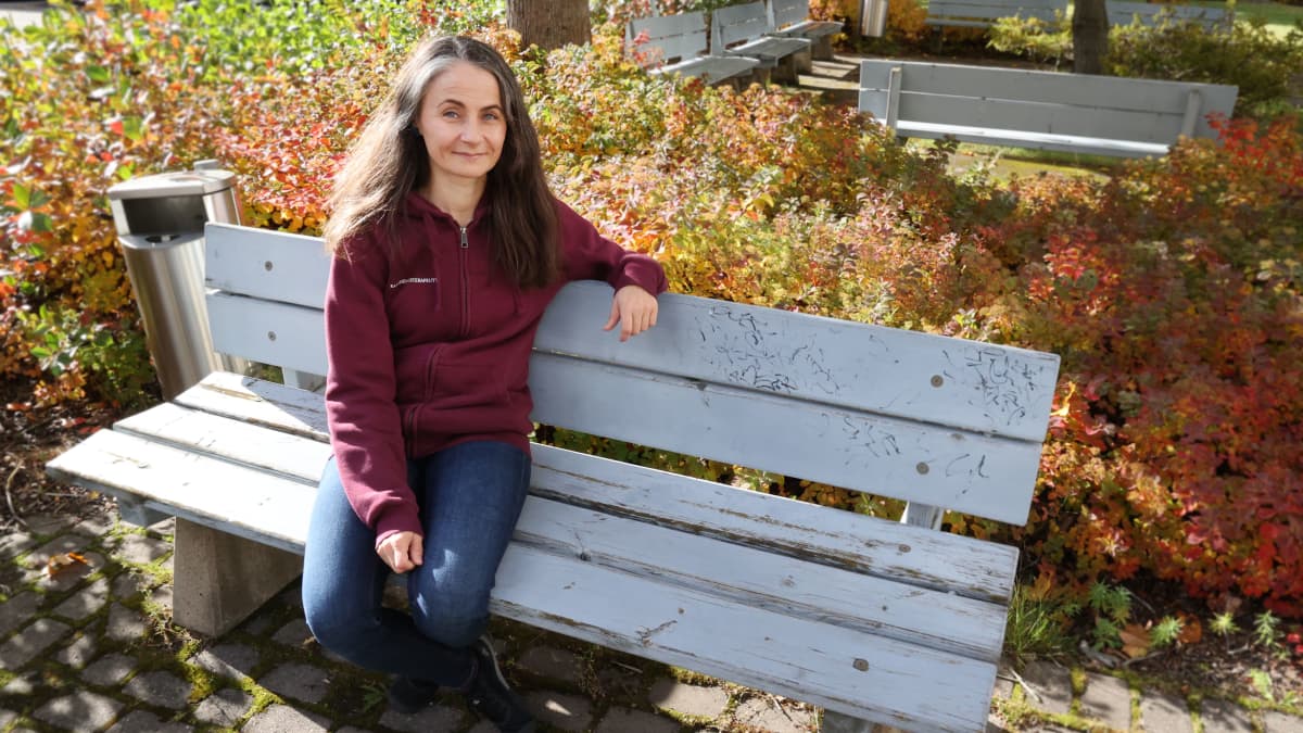 Ravitsemusterapeutti Marjaana Puustinen istuu puiston penkillä käsi rennosti penkin selkänojalla.