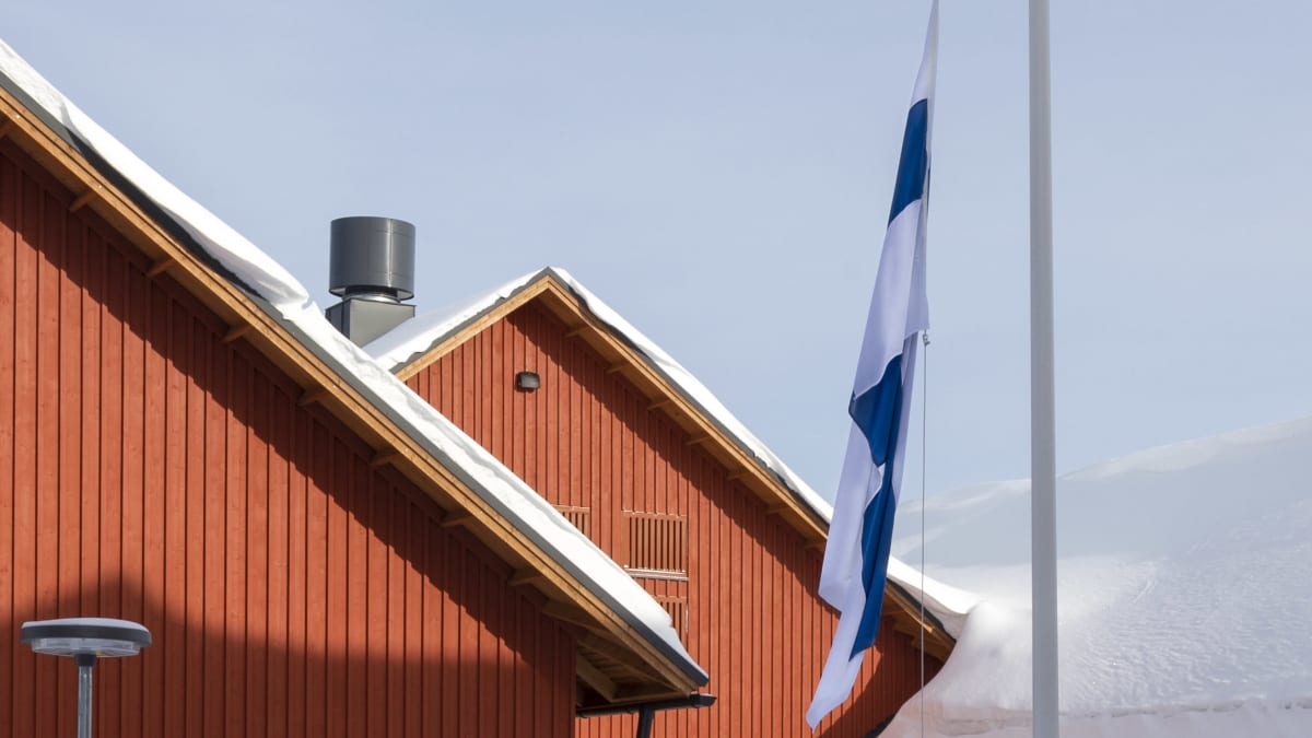 Suomen lippu on puolitangossa Humakin Korpilahden oppilaitoksen pihalla. Taustalla näkyy punaisia puurakennuksia. 