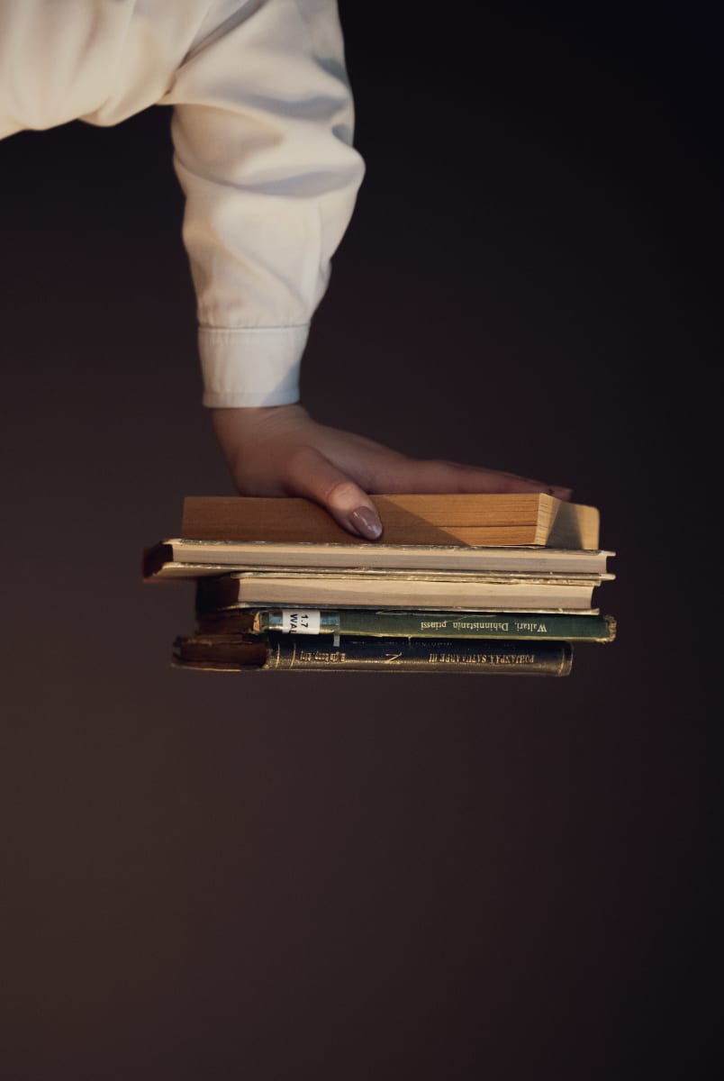 Kädessä pino kirjoja ylösalaisin.