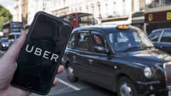 Kännykän ruutu, jolla Uber-sovellus, taustalla musta taksi