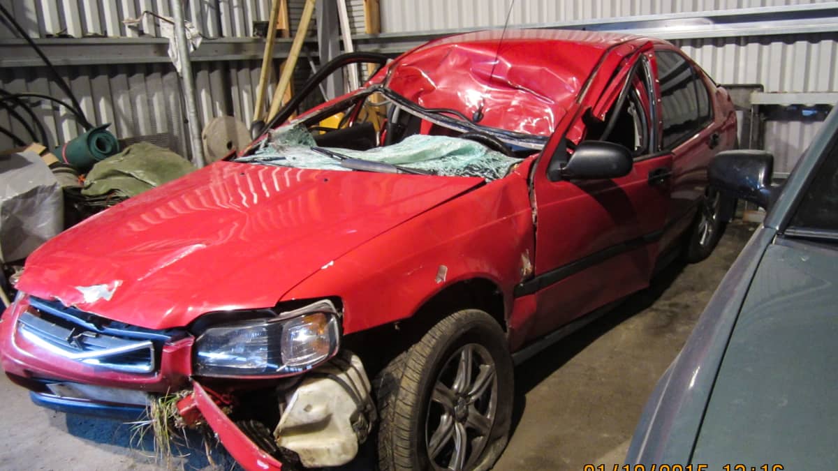 Autotallissa auto, jota Toni Manninen ajoi menehtyessään hirvikolarissa. Auton katto on painunut etuosastaan alas. Auton keulasta roikkuu osia ja eturengas on tyhjä. 
