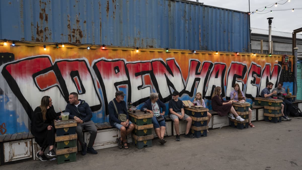 Ihmisiä istumassa pöytien ääressä suuren Kööpenhamina-graffitin edessä.
