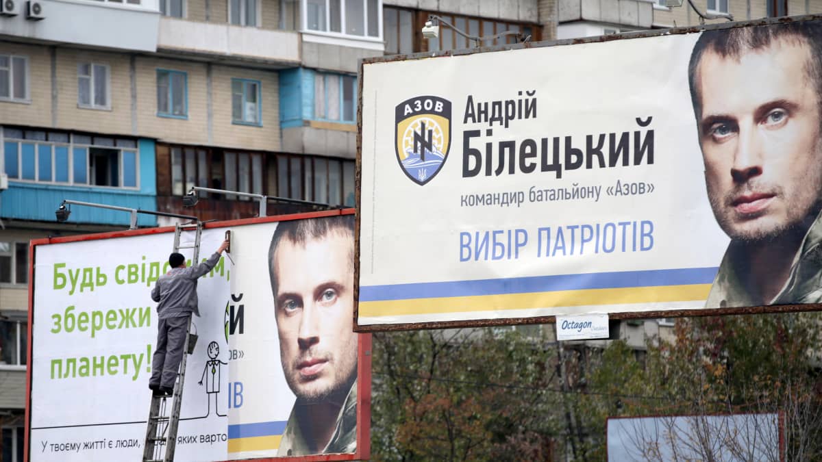 Työntekijä kiinnittää mainostauluun Azovin rykmentin komentajan Andrii Biltskin vaalimainosta.