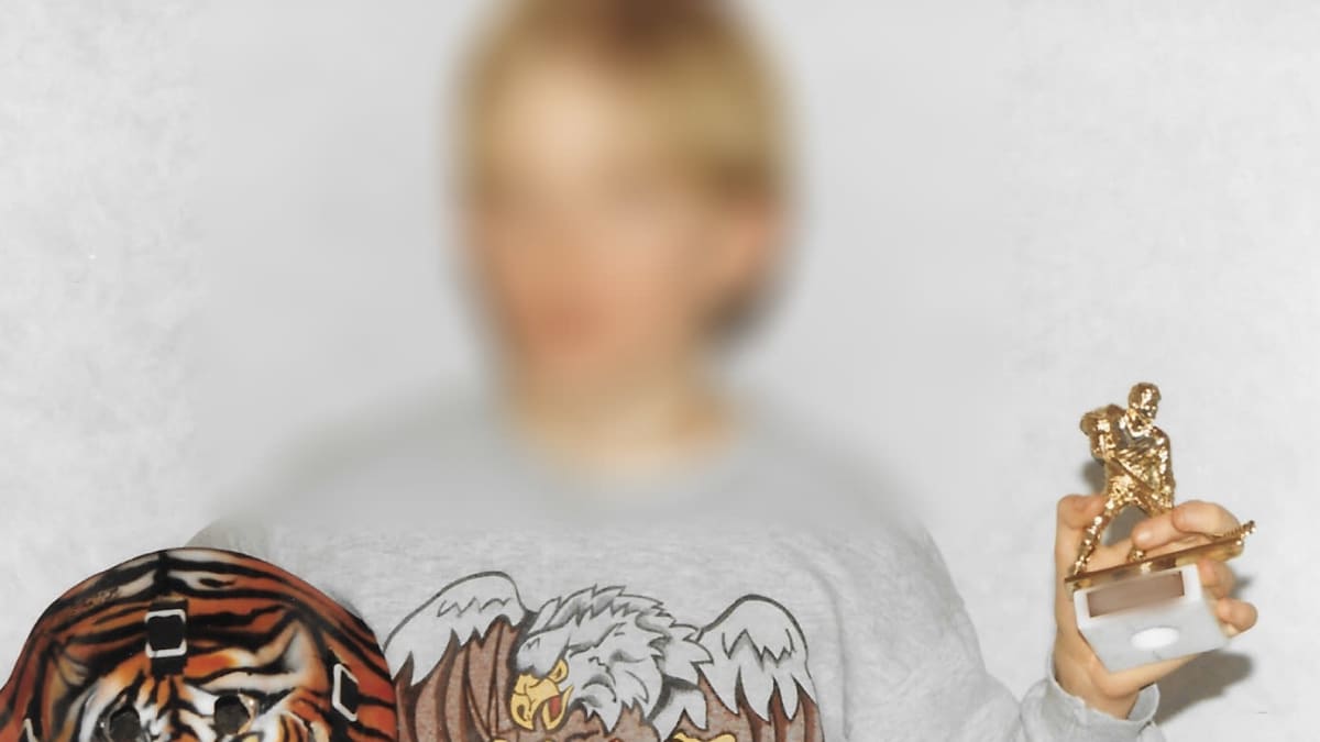 Kuva nuoresta pojasta, joka pitää kädessään jääkiekkoilijapatsasta ja jääkiekkomaalivahdin kypärää, jossa on tiikerinkasvot kuviointina. Pojan kasvot on sumennettu anonyymiteetin vuoksi.