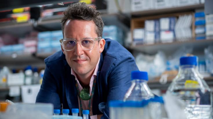 Professori Matthew Kemp poseeraa kameralle sinisessä puvuntakissa.