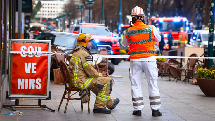 Palomies istuu tuolilla ja juttelee ensiapuhenkilöstön kanssa onnettomuuspaikalla Pohjoisesplanadilla. 
