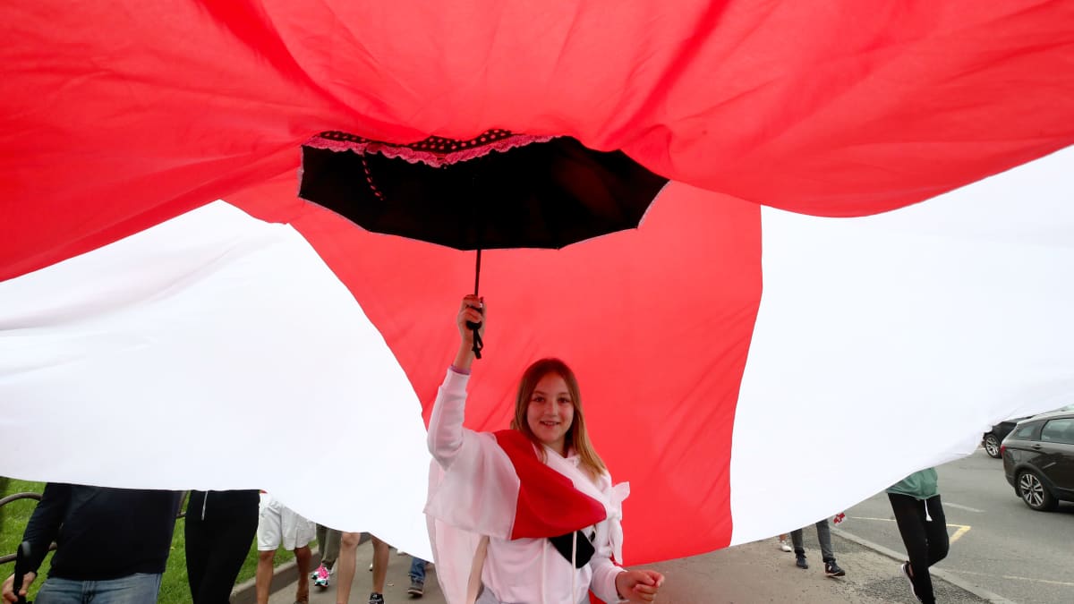 Nainen kannatteli sateenvarjolla suurta punavalkoista kangasta Minskissä Valko-Venäjällä ennen suurmielenosoituksen alkua 6. syyskuuta 2020. Punavalkoinen lippu on noussut opposition symboliksi mielenosoituksissa.