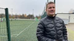 Lasse Peltonen nojaa kaiteeseen kentän laidalla. Taustalla näkyy jalkapallokenttä ja koululaisia.