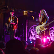 Rock-yhtye esiintyy lavalla, taustalla näkyy laulaja-basisti Elli Haloo (Elisa Tiilikainen) ja kitaristi Jere Marttila