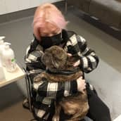 Nainen istuu eläinlääkärin vastaanotolla koira sylissään. 