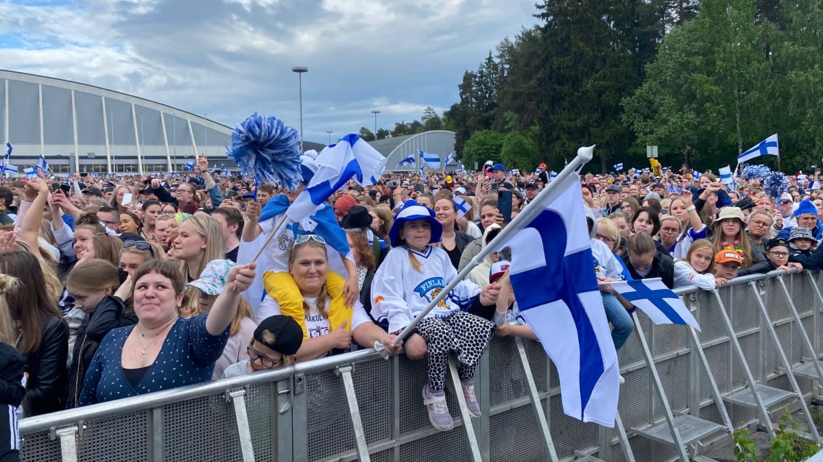 Hakametsän parkkialue täynnä ihmisiä. Etualalla eturivissä lapsia heiluttamassa Suomen lippuja.