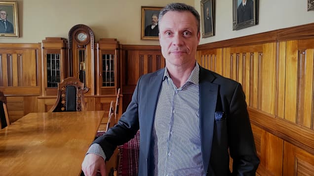 En man som står i ett rum med träpaneler på väggarna. 