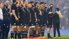 Uuden-Seelannin rugbymaajoukkue rivissä kuuntelemassa kansallislaulua. Rivin viimeisenä seisoo ylimääräinen henkilö, jota ollaan poistamassa kentältä.