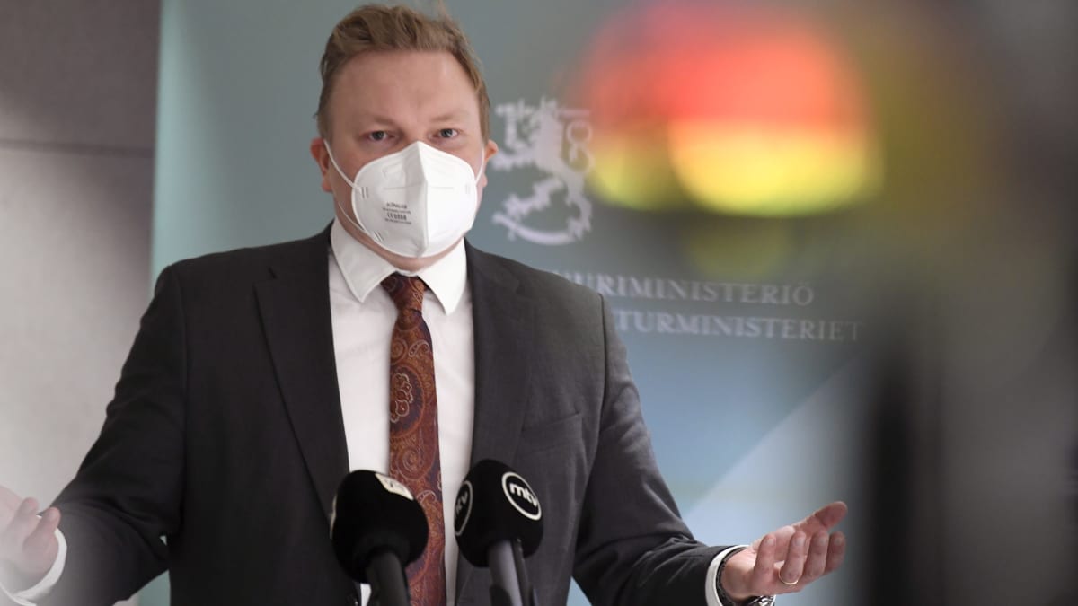 Antti Kurvinen under ett presstillfälle. Han bär ett vitt munskydd.
