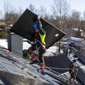 Solarvoima Oy:n asentaja Joni Särkinen kantaa aurinkopaneeleja omakotitalon katolle.