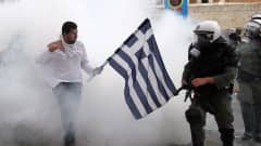 Grekisk man som håller flagga framför kravallpoliser