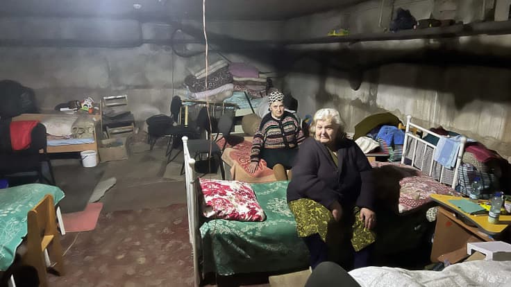 Kaksi iäkästä naista istuu sängyillä kellarissa.