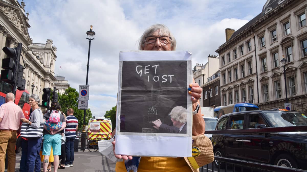 Nainen pitelee kylttiä, jossa on Boris Johnsonin kuva ja englanniksi kirjoitettu häivy-kehotus.