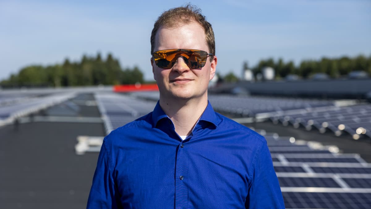 Mies aurinkolasit päässään Hämeenlinnan prisman katolla. Paljon aurinkopaneeleja taustalla.