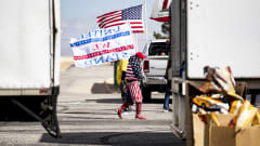 Yhdysvaltain lipun väreihin ja kuvioihin pukeutunut henkilö kantaa lippua rekkojen edustalla.
