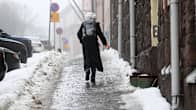 Woman seen from behind walking up a city sidewalk covered in ice. 