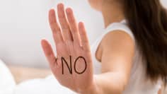 En kvinna med ansiktet bortvänt som har text "No" skriven i handflatan som hon vänder mot kameran. 