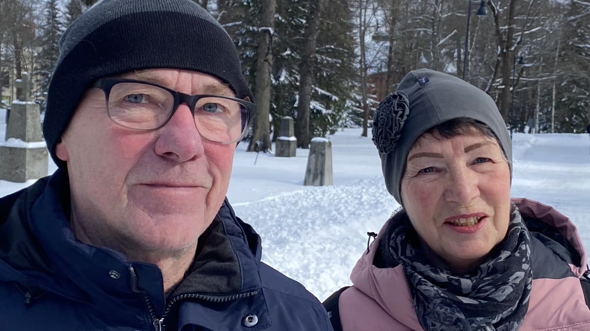 Ulkovaatteisiin pukeutuneet Ari Hevonkorpi ja Lea Leinonen katsovat kameraan hymyillen. Taustalla näkyy lumista hautausmaa-aluetta.