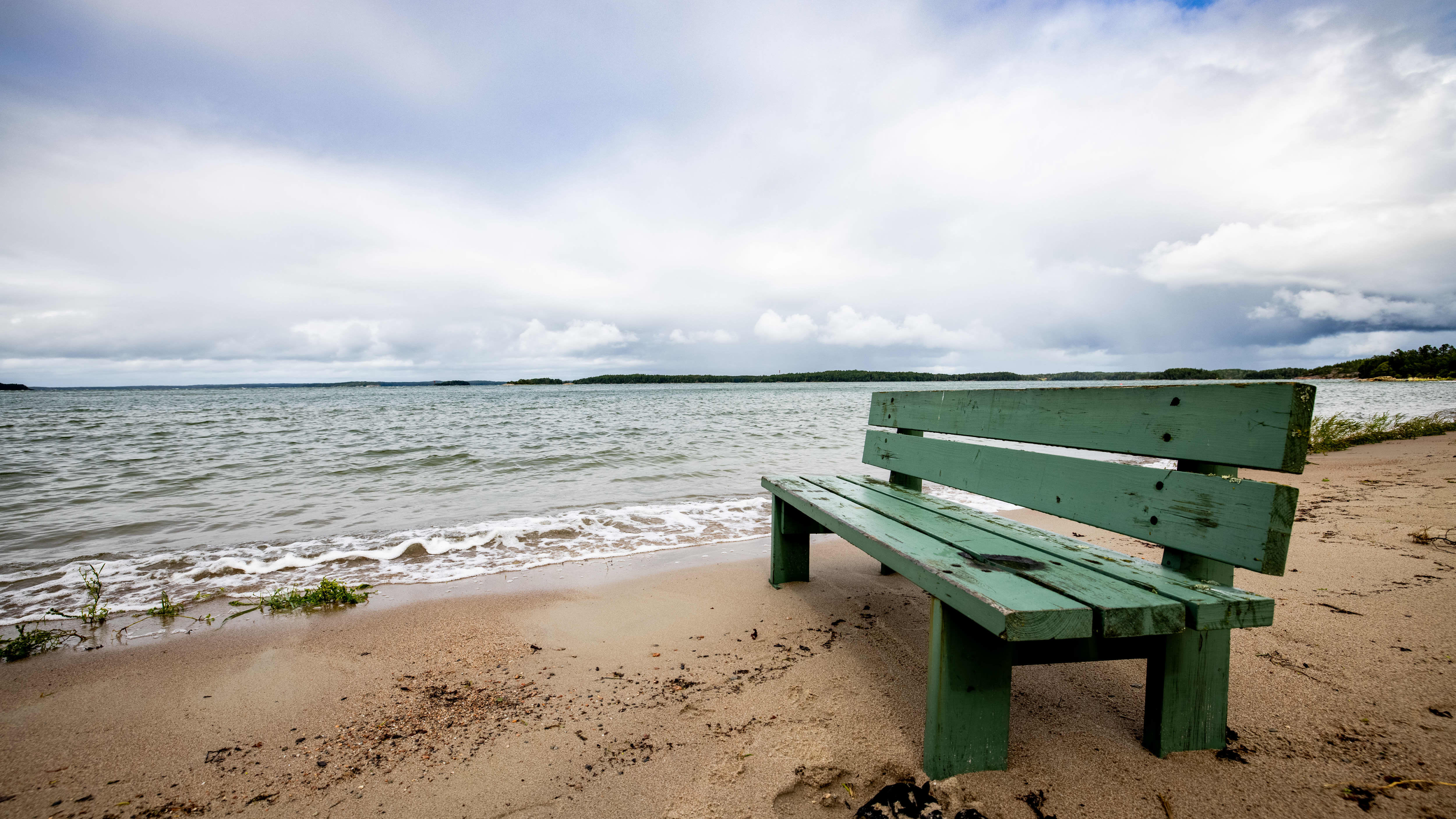 Hijaisella uimarannalla tyhjä penkki pilvisellä säässä.