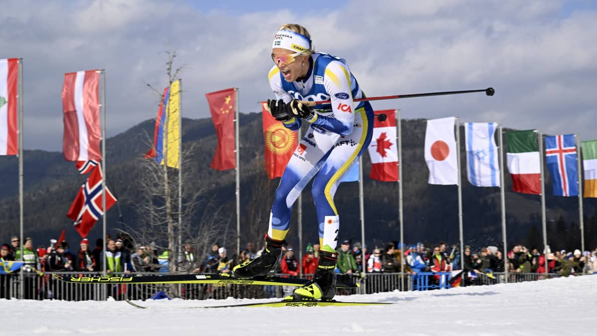 Frida Karlsson hiihtää Planican MM-kisoissa. Taustalla näkyy eri maiden lippuja.