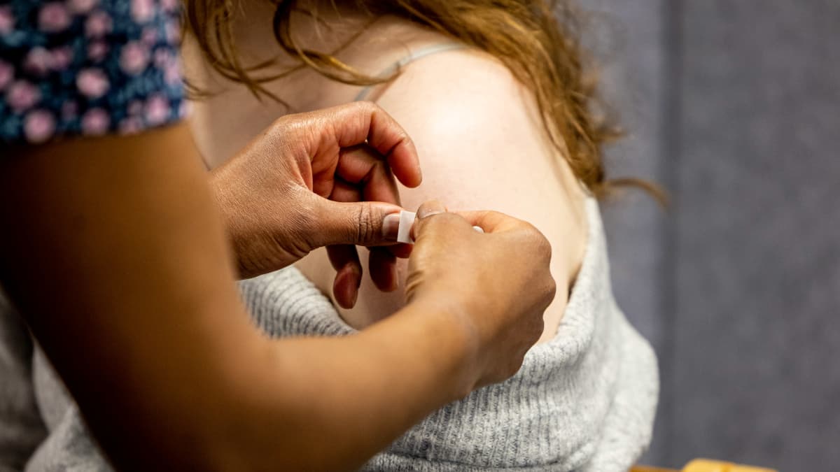 Rokottaja laittaa laastaria henkilön rokotuskohtaan olkapäähän.