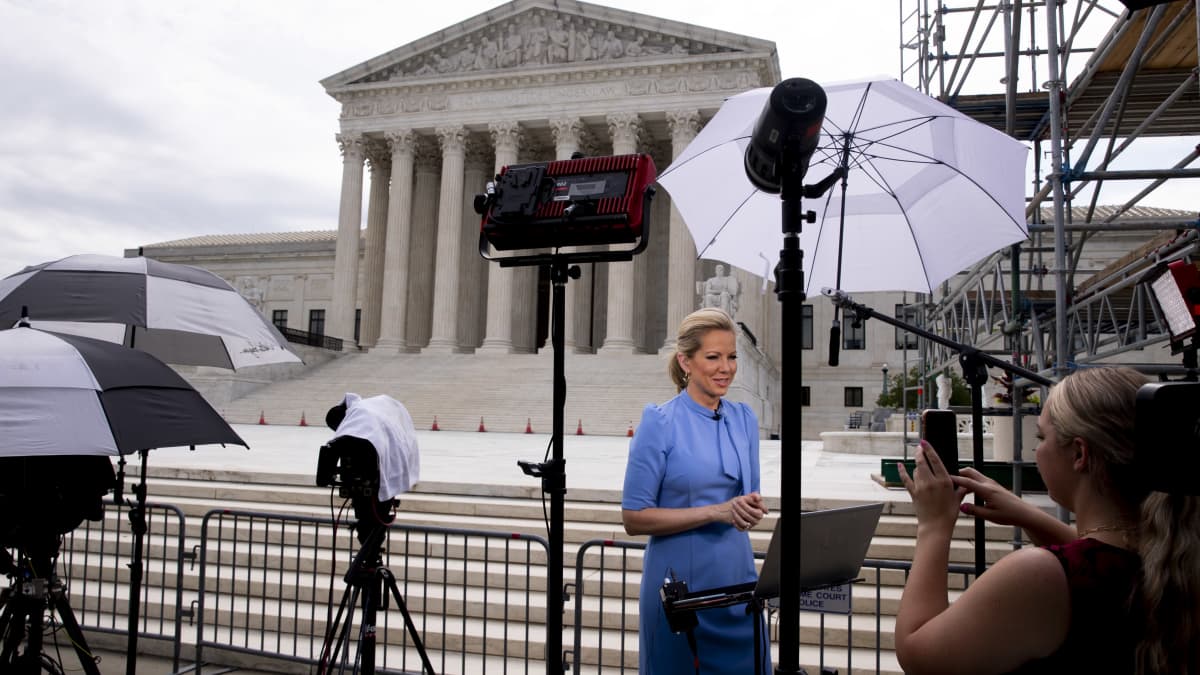 Uutistoimittaja nainen seisoo kameran edessä, taustalla Yhdysvaltain korkeimman oikeuden rakennus. 