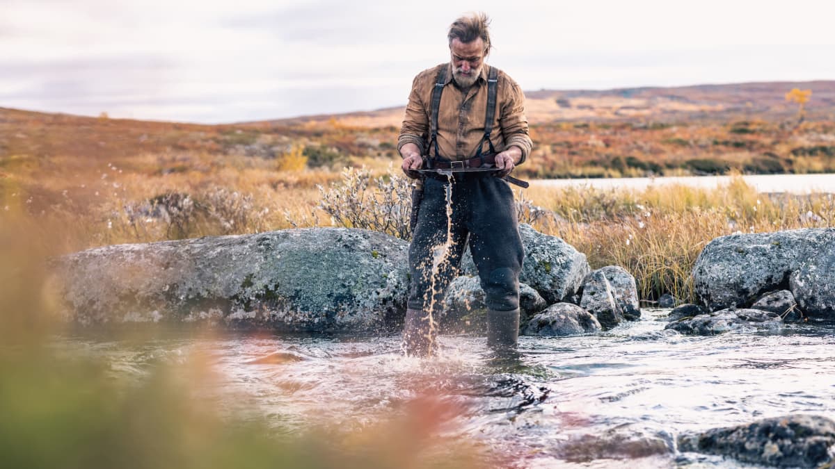 En ensam man vaskar efter guld stående i en fjällbäck. 